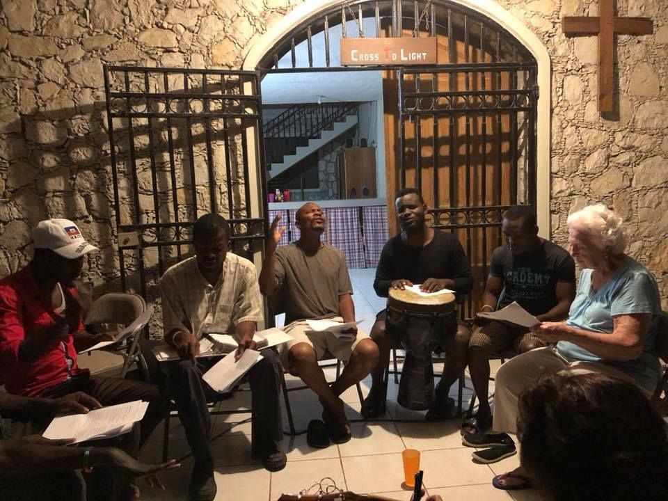 A group of people are sitting in a circle in front of a stone wall.