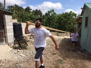 A man in a white shirt is carrying a large piece of wood.