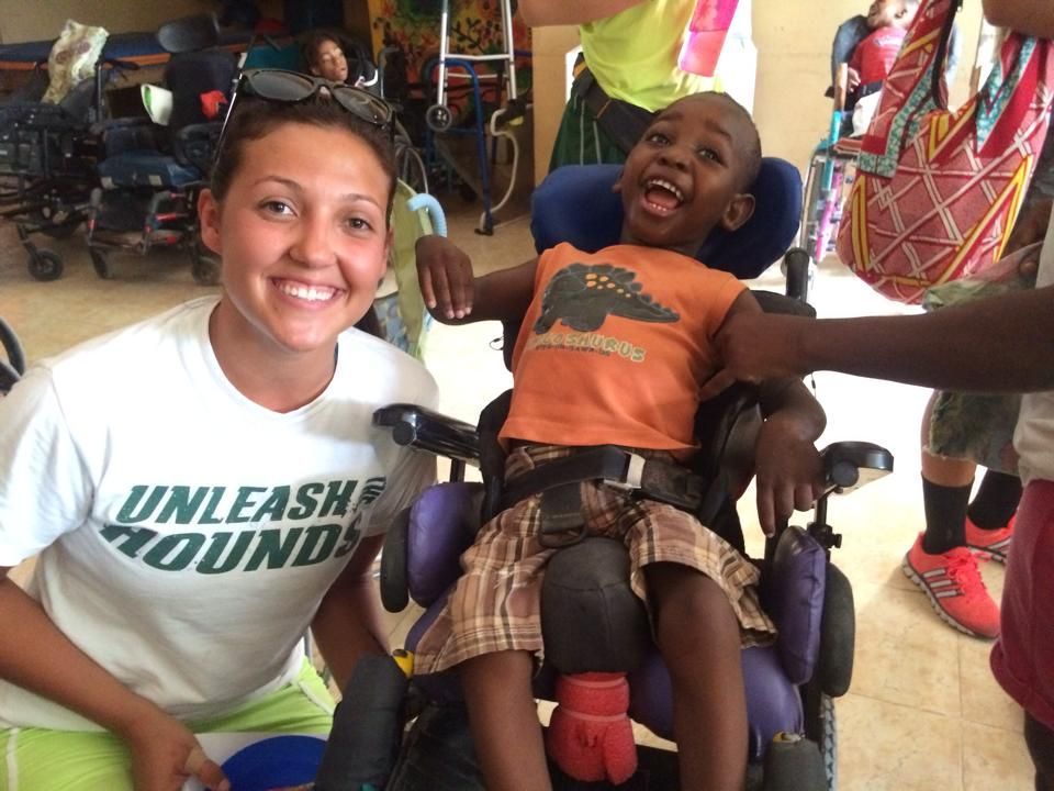 A girl wearing a shirt that says unleash round is standing next to a boy in a wheelchair