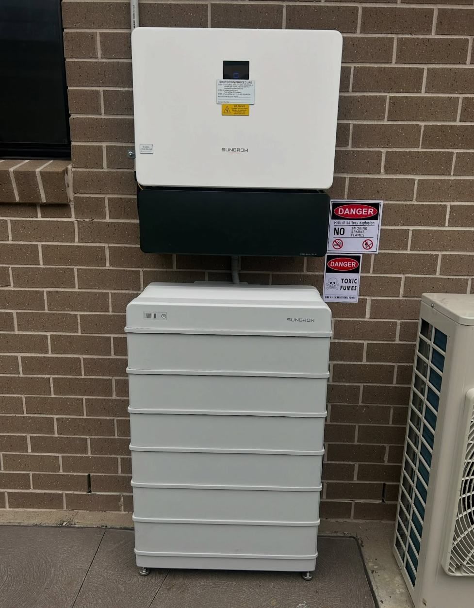 A White Battery Box is Sitting in Front of a Brick Wall — DLG Electrical and Solar In Hunter Valley, NSW