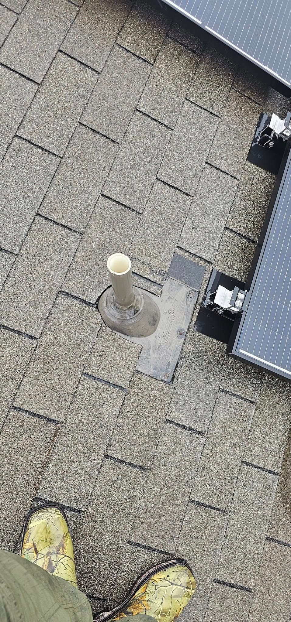 A person is standing on a roof next to a solar panel.