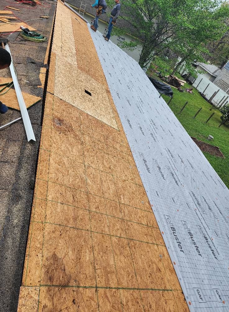 A man is standing on top of a roof covered in plywood.