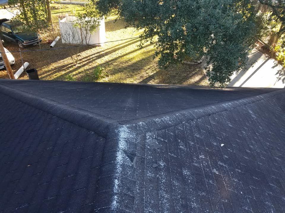 A black roof with trees in the background and a car parked on the side of it.