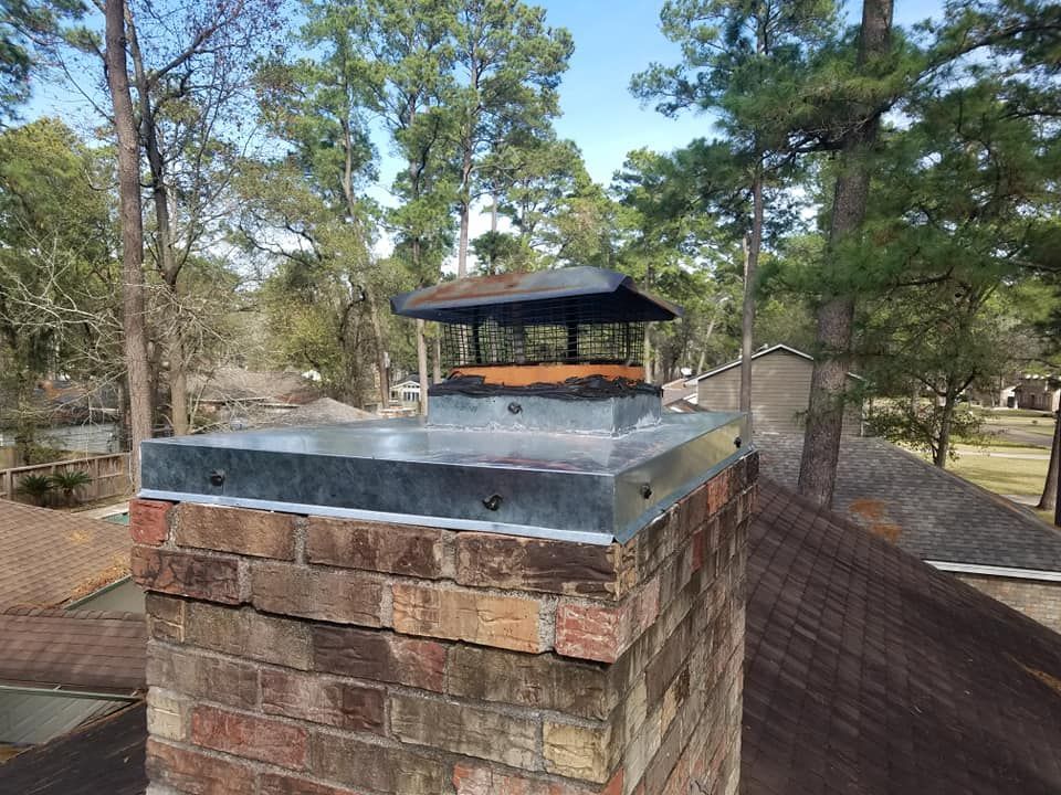 A brick chimney on top of a roof with trees in the background.