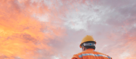 A construction worker is standing in front of a sunset sky.
