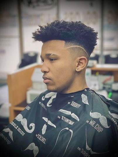 Man with high-top fade haircut and shaved side design, wearing barber's cape.