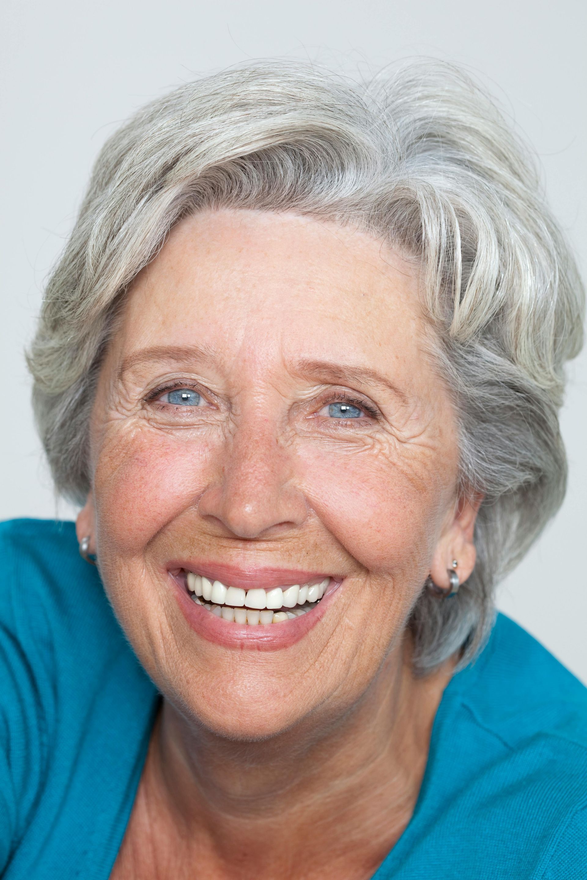 An older woman with gray hair and blue eyes is smiling for the camera.