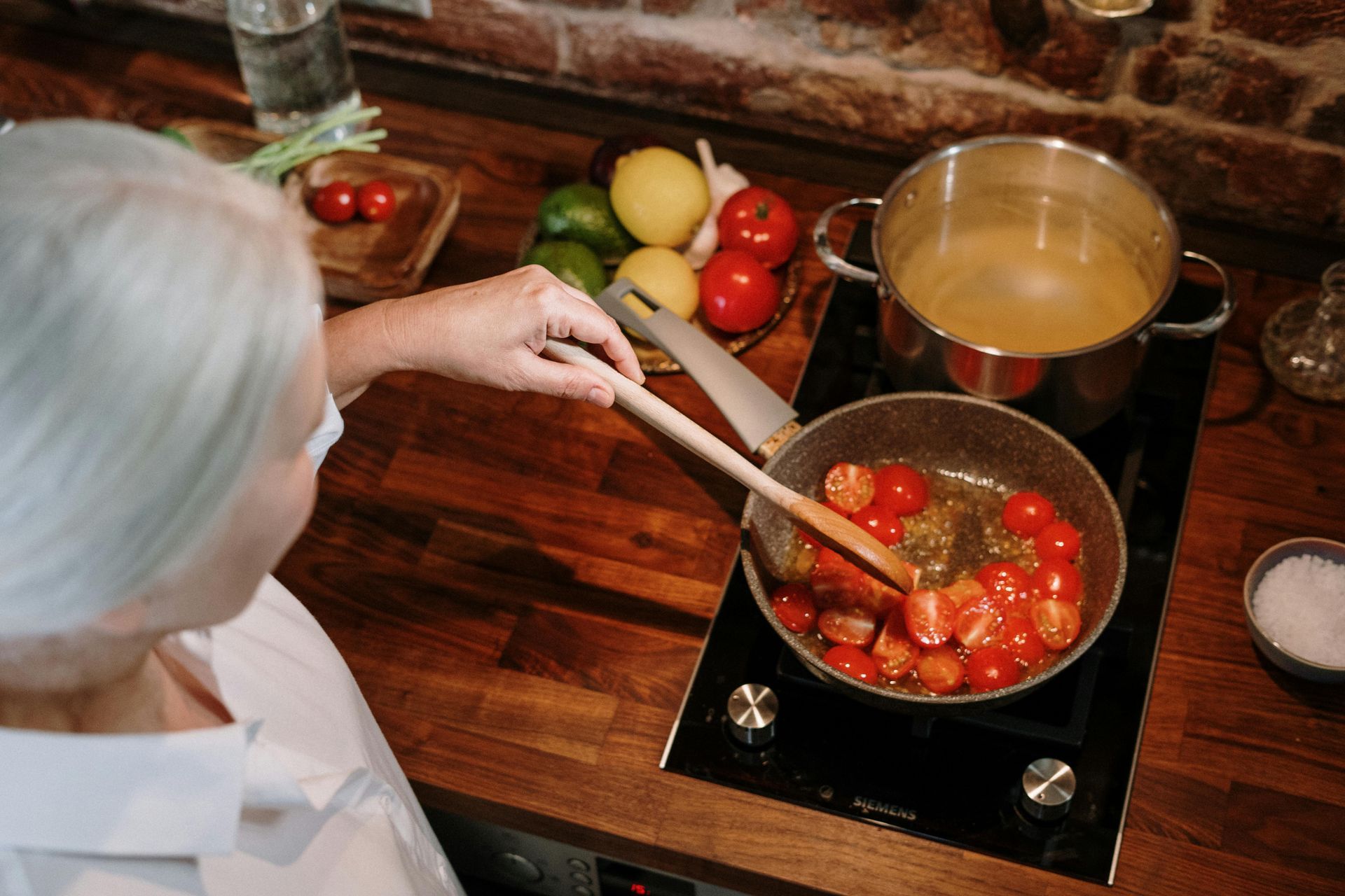 A woman is cooking tomatoes in a frying pan on a stove.