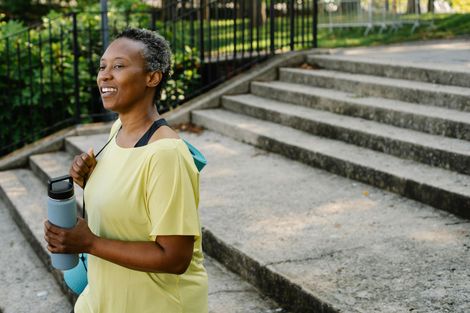 A woman is walking down a set of stairs holding a yoga mat and a water bottle.