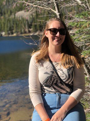 A woman wearing sunglasses is sitting in front of a lake.