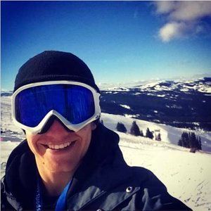 A man wearing goggles and a black hat is smiling in the snow