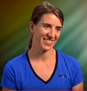 A woman is wearing a blue fila shirt and smiling.