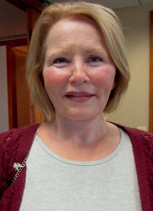A woman wearing a red sweater and a white shirt is smiling for the camera.