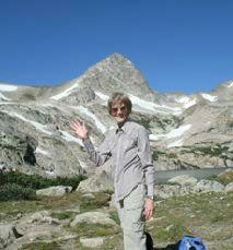 A man is standing in front of a mountain waving his hand.