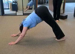 A woman is doing a downward dog yoga pose in a gym.