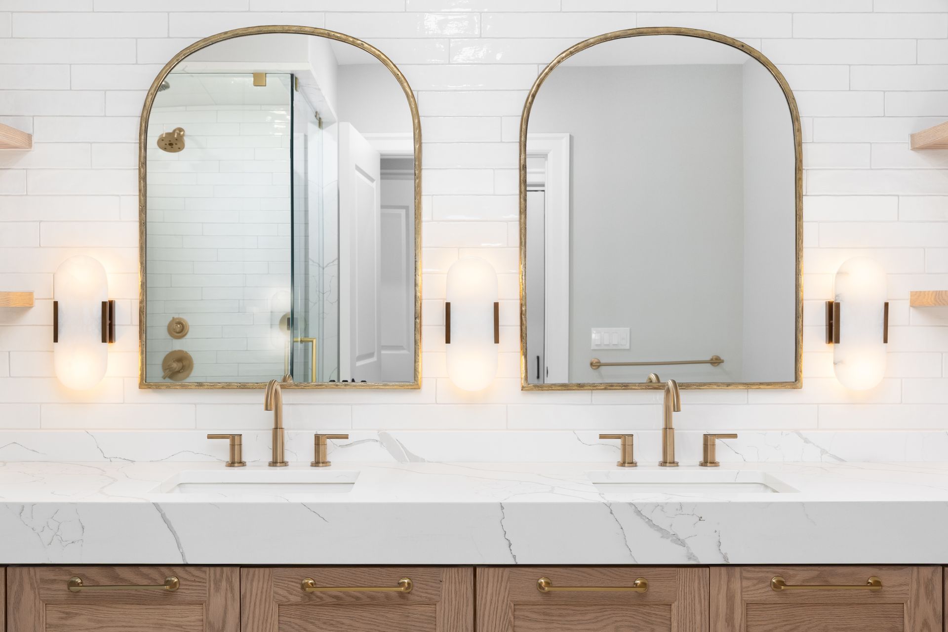 Two large mirrors mounted on a wall in a bathroom with white tiled walls and matching faucets. Two large mirrors mounted on a wall in a bathroom with white tiled walls and matching faucets.
