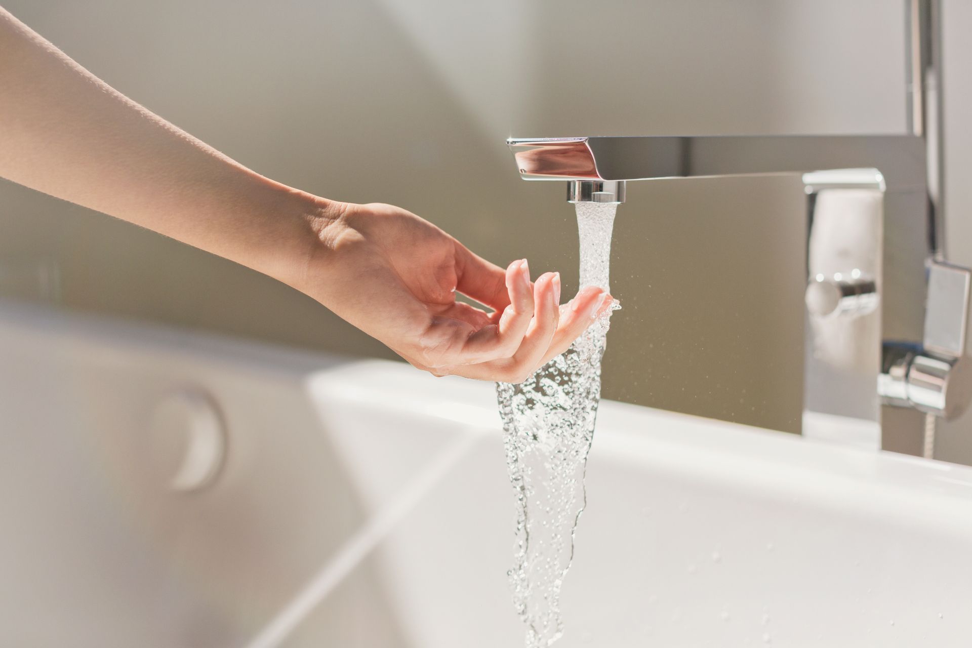 Hand held under running water from a modern bathroom sink faucet.