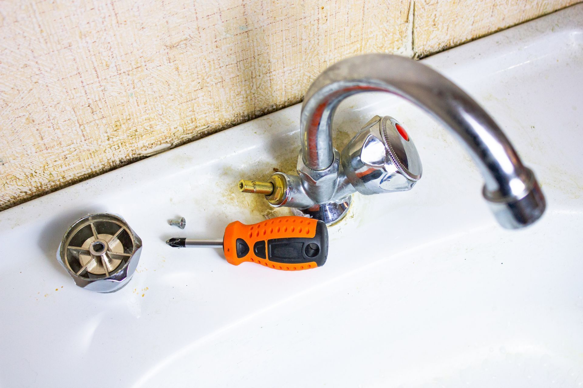 Bathroom sink with a chrome faucet, drain, and an orange-handled screwdriver lying on the basin.