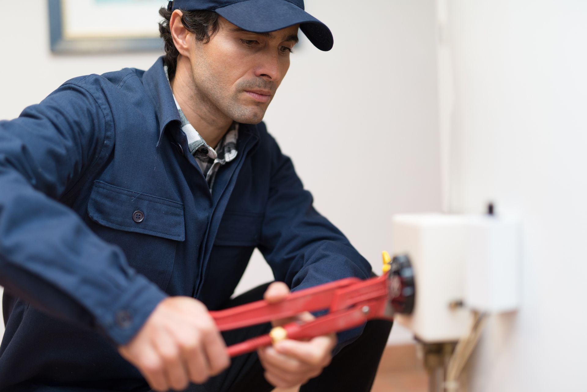 Technician in blue uniform using a red pipe wrench near a wall fixture