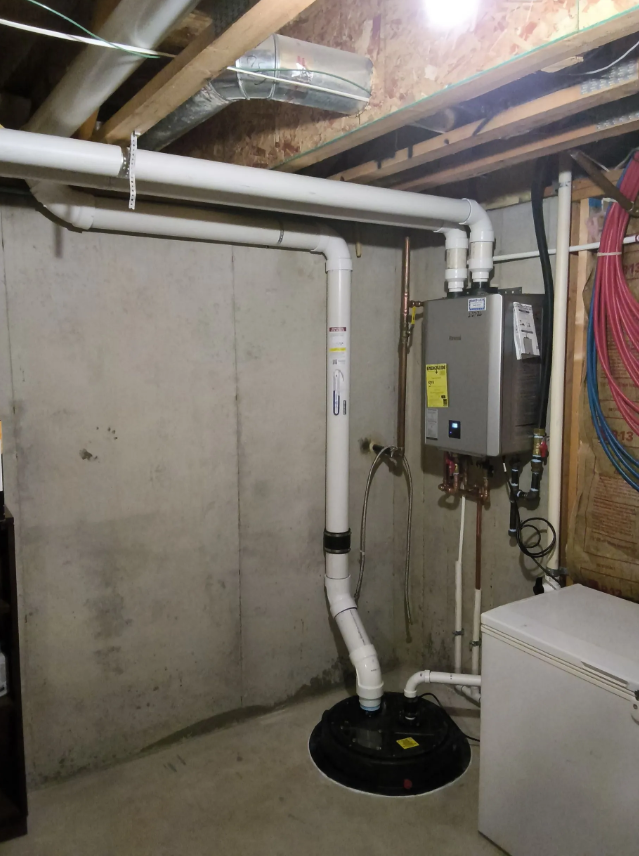 Basement utility area with white pipes, electrical panel, and black sump pump lid on the floor.