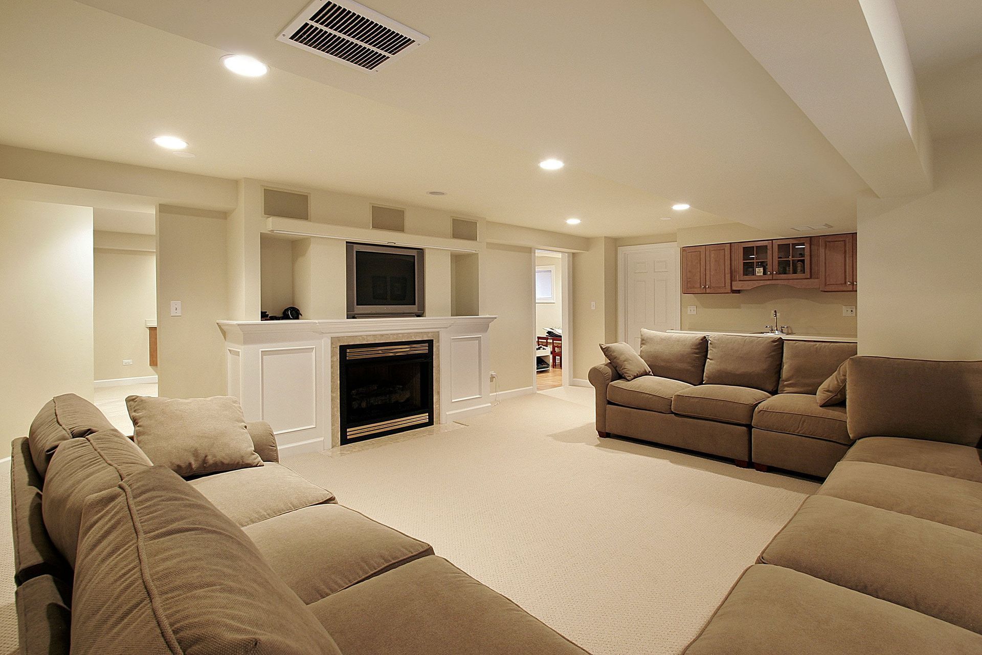 Spacious beige living room with sectional sofas, fireplace, TV, and recessed lighting