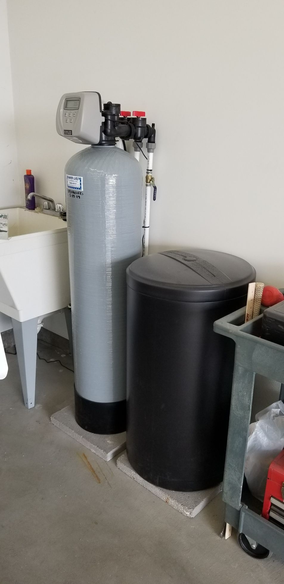 Gray water softener tank and black storage tank beside a utility sink in a basement.