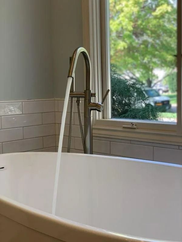 Bathtub beneath a tall chrome faucet by a window with a green outdoor view