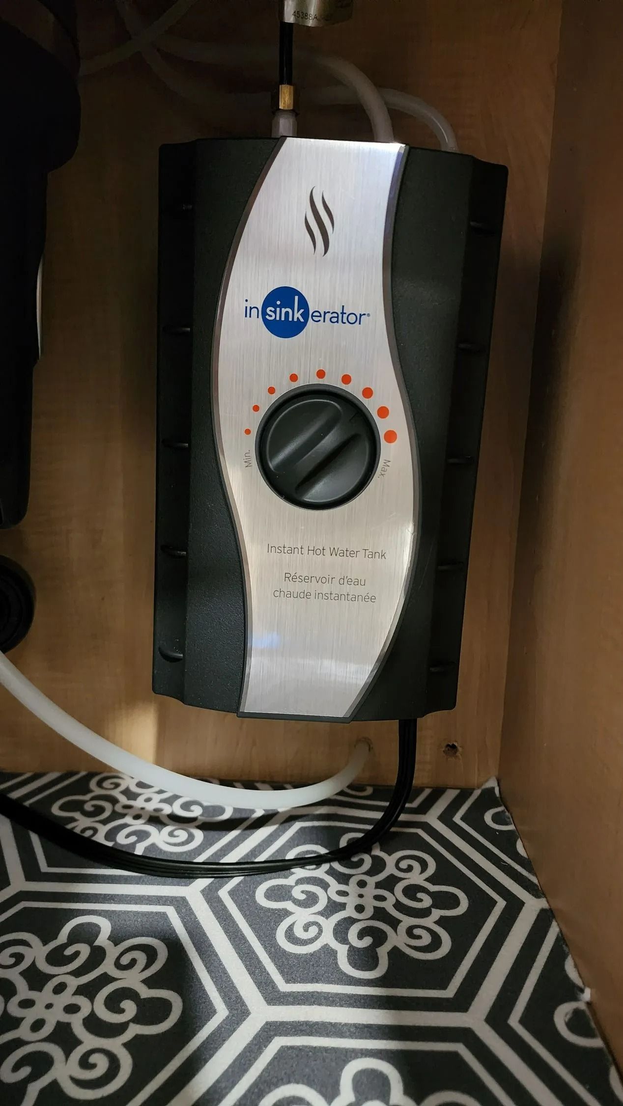 Compact white control unit with a black dial, mounted above a patterned floor in a wooden cabinet.