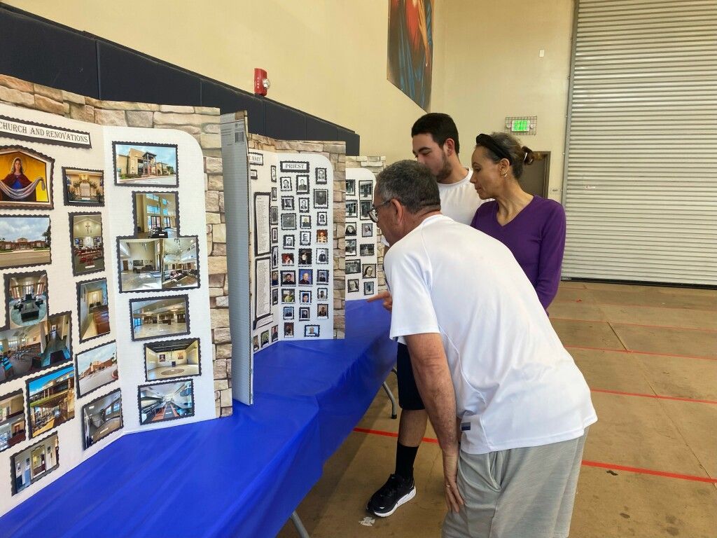 Three people viewing display boards on a blue table at an indoor exhibition
