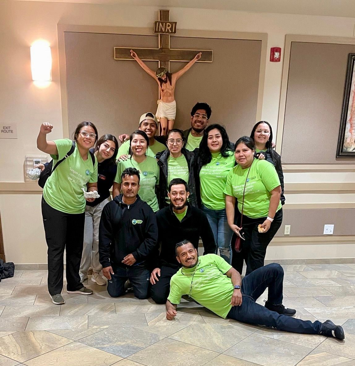 Group posing in a church, most wearing bright green shirts, with a crucifix in the background.