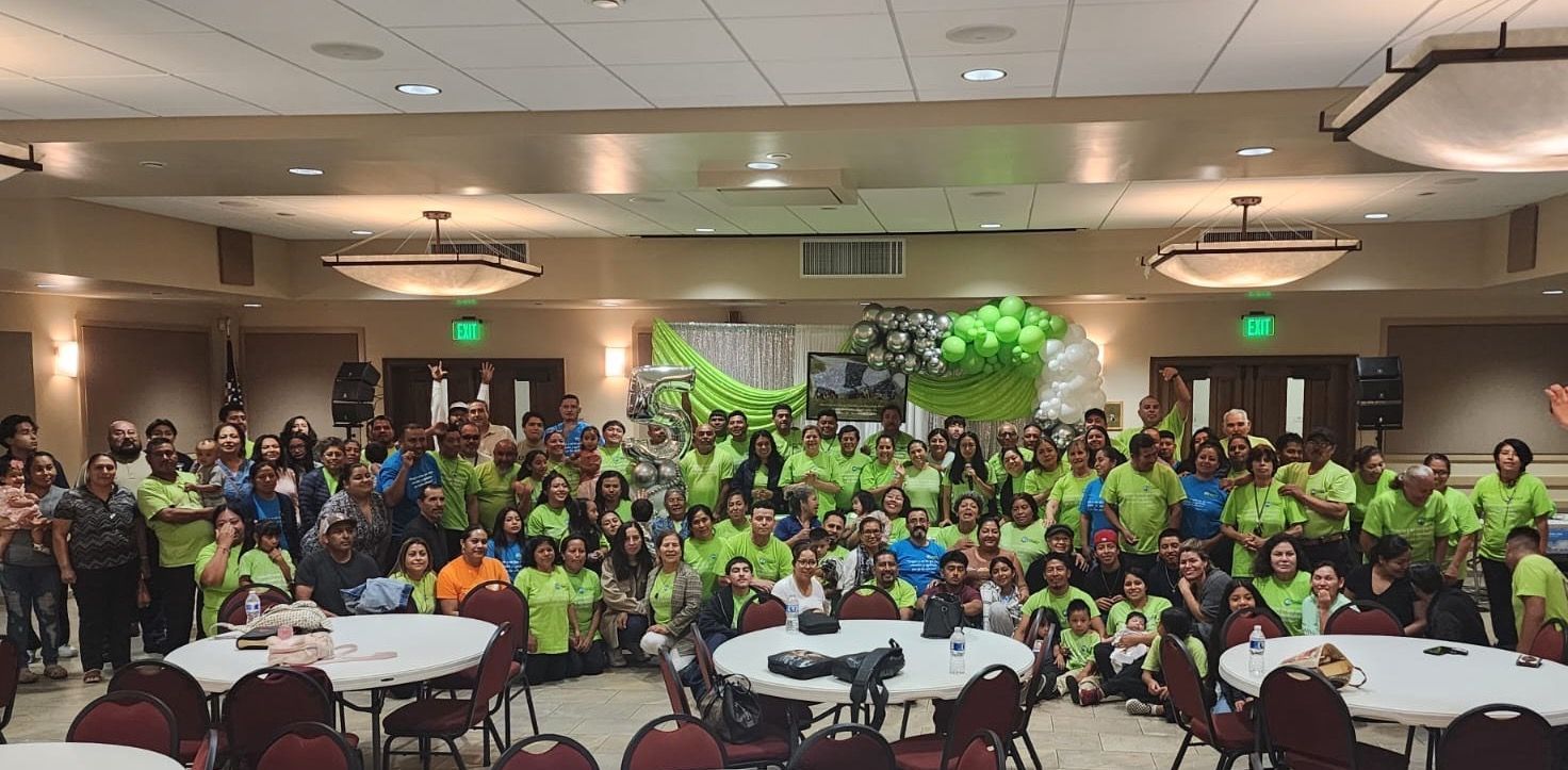 Large group in bright green shirts posing in a banquet hall with round tables and ceiling lights