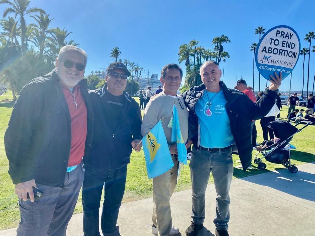 Four people posing outdoors at a rally, with a sign reading “Pray to End Abortion.”