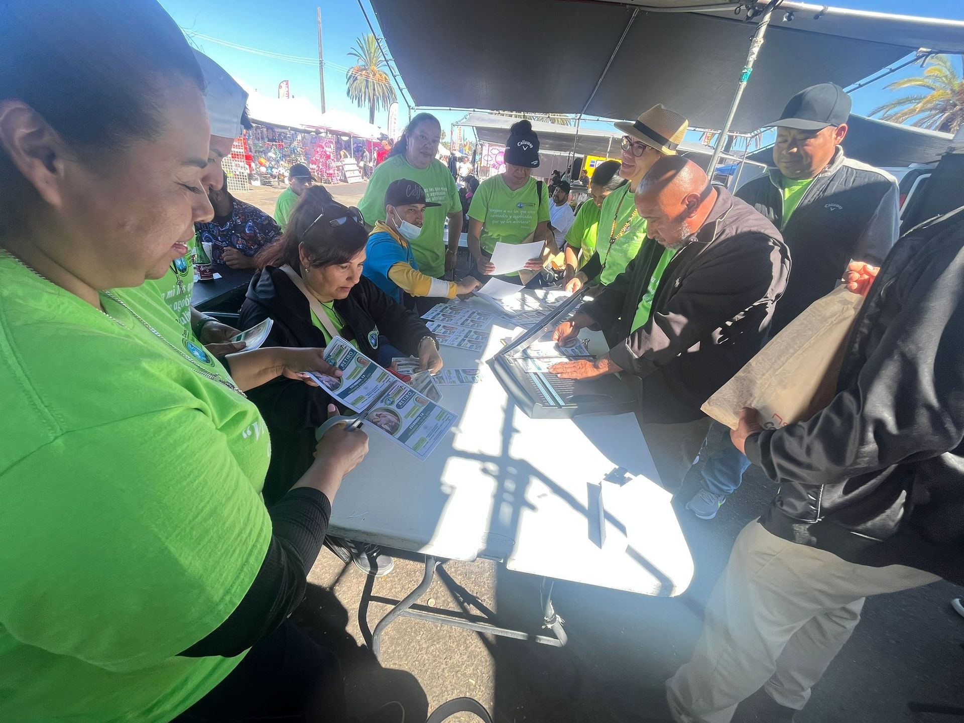 People in bright green shirts gather around a table under a canopy at an outdoor event.