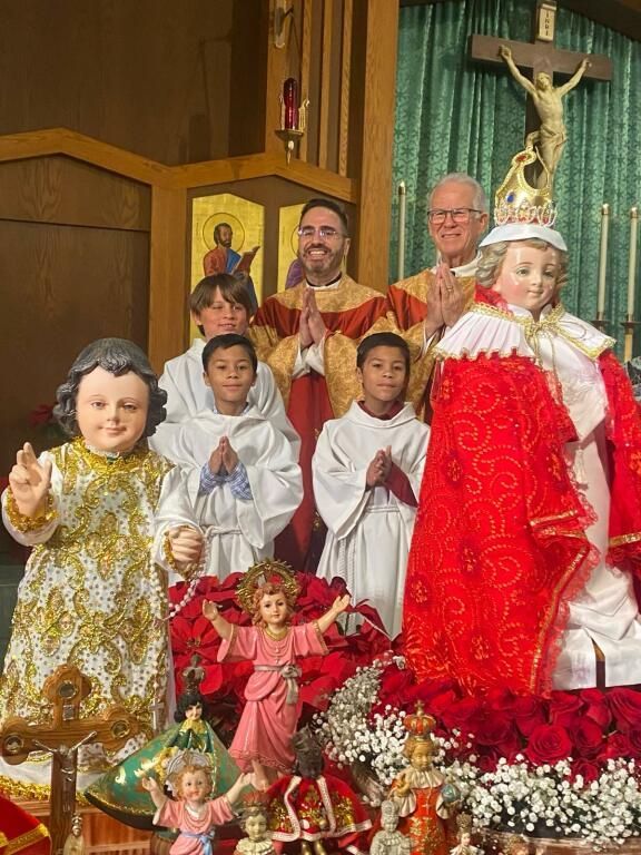 Two men and children posed in a church with religious statues and flowers