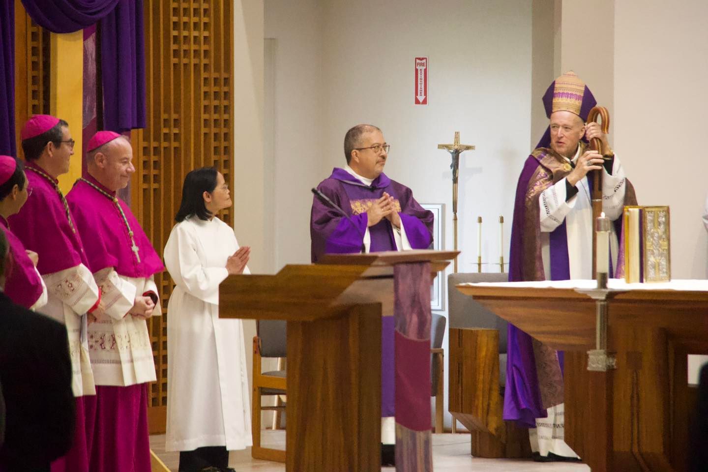 Clergy in purple vestments conduct a church service beside an altar and lectern.