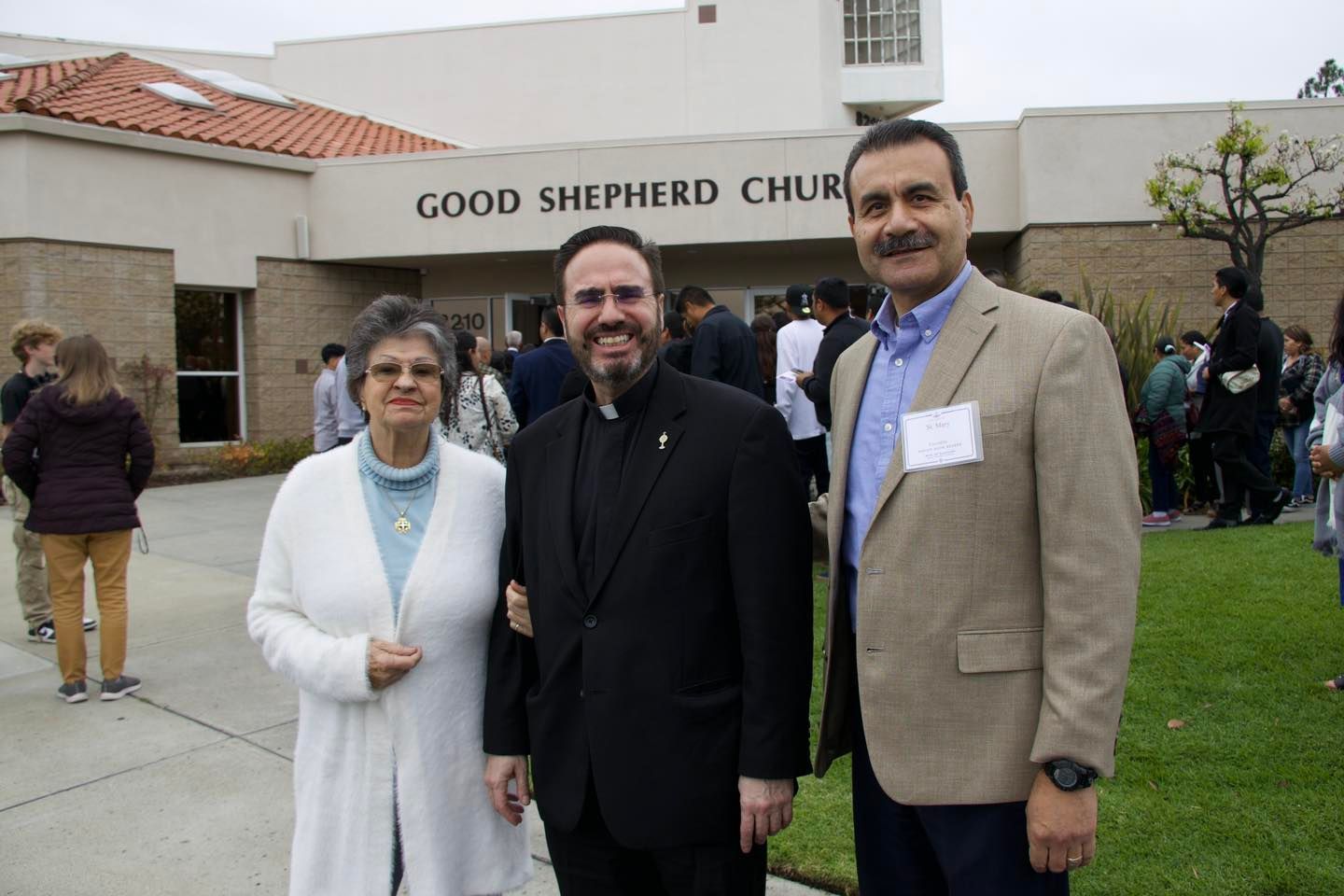 Three people posing outside Good Shepherd Church on a grassy lawn.