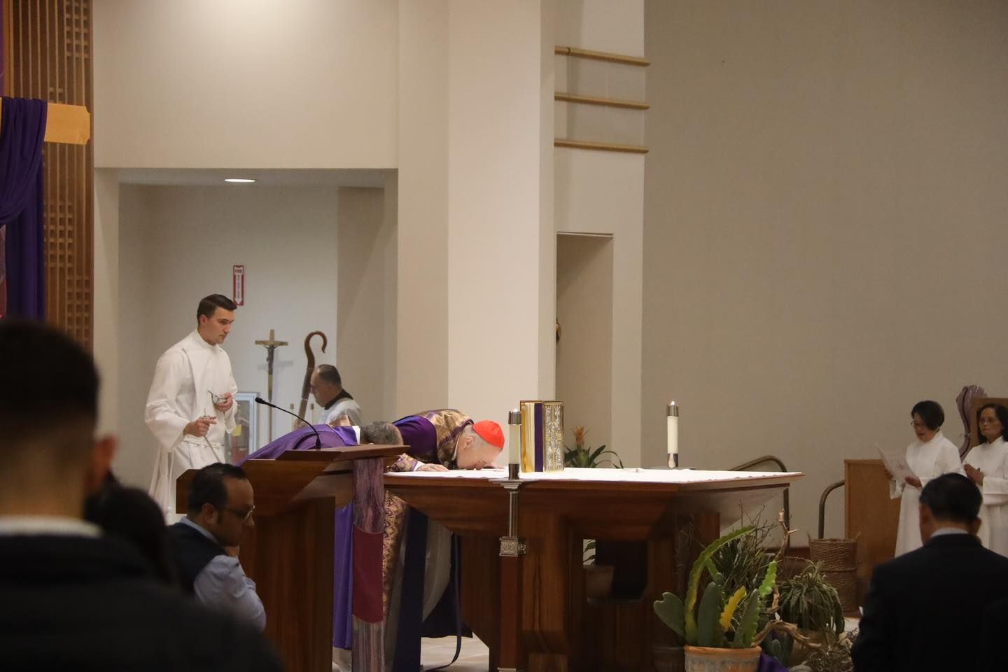 Priest at altar during church service, with choir members seated nearby