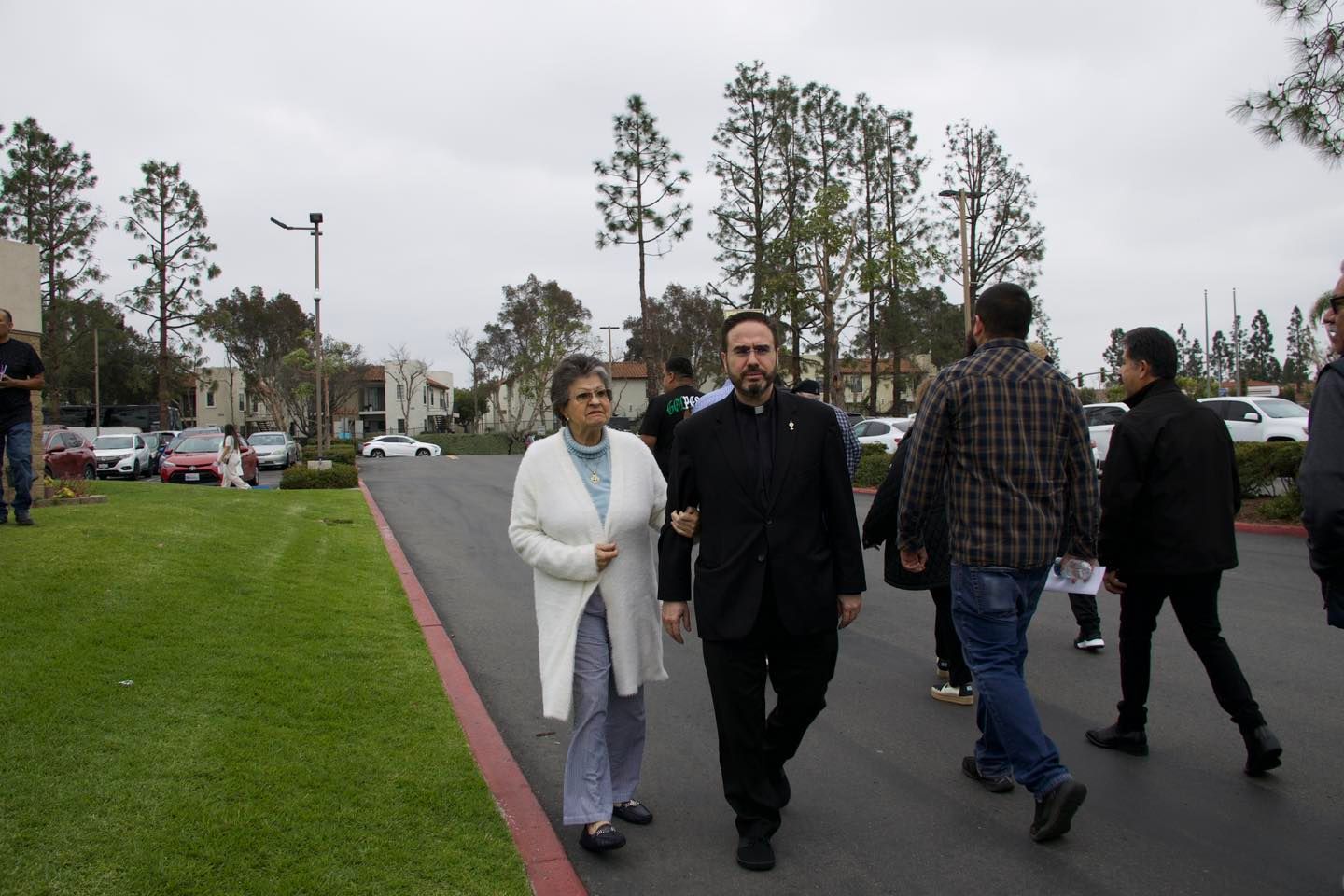 People walking along a paved path beside a grassy area on an overcast day.