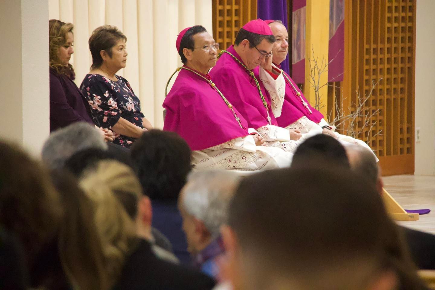 Clergy in pink robes seated at a church ceremony, viewed from the audience