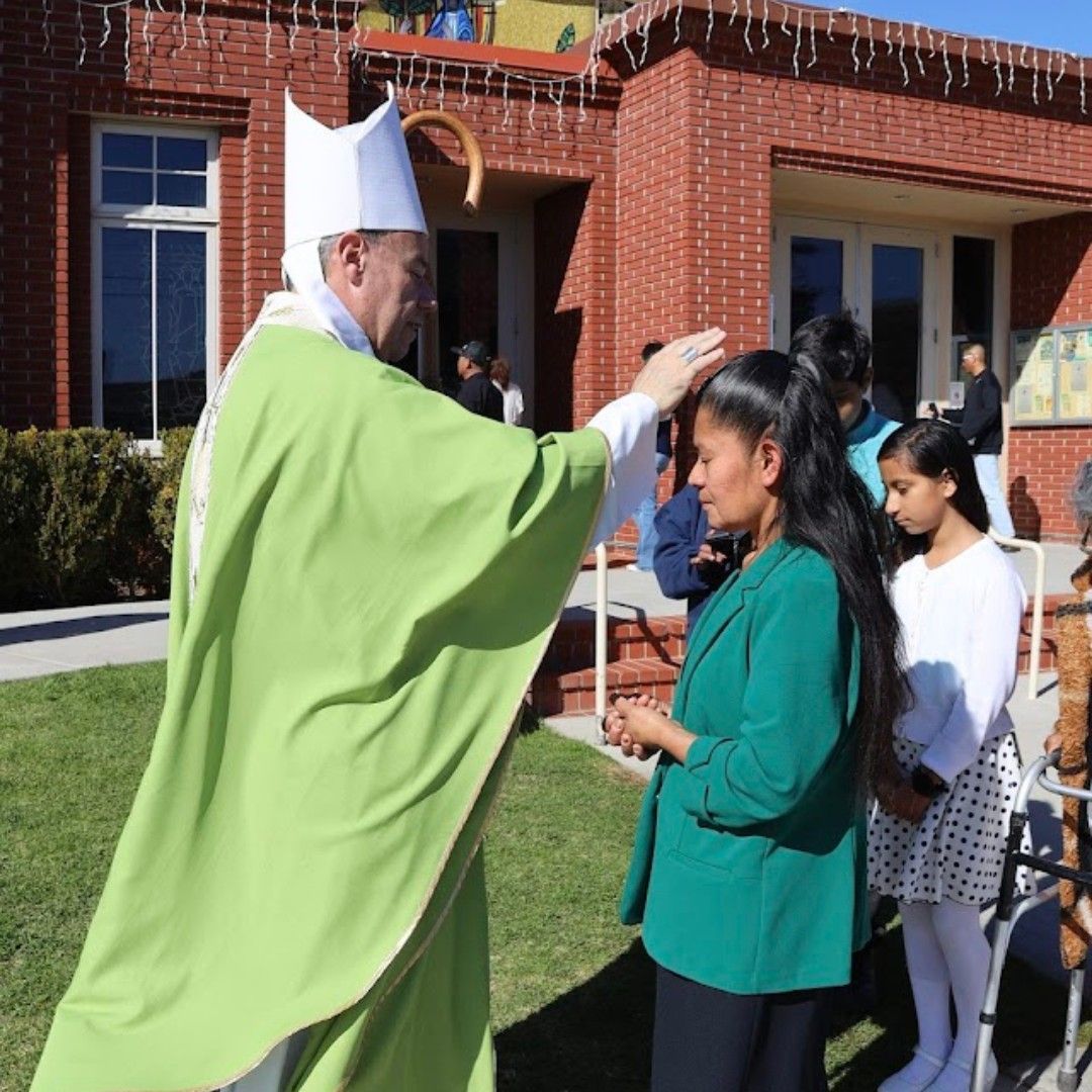 Priest in green vestment blessing children outside a brick building