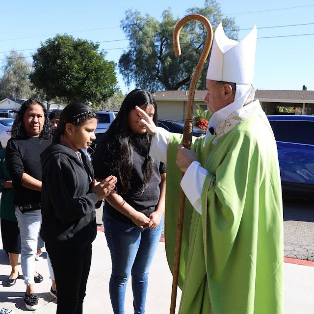 A bishop in green robes blesses people outdoors with a staff.