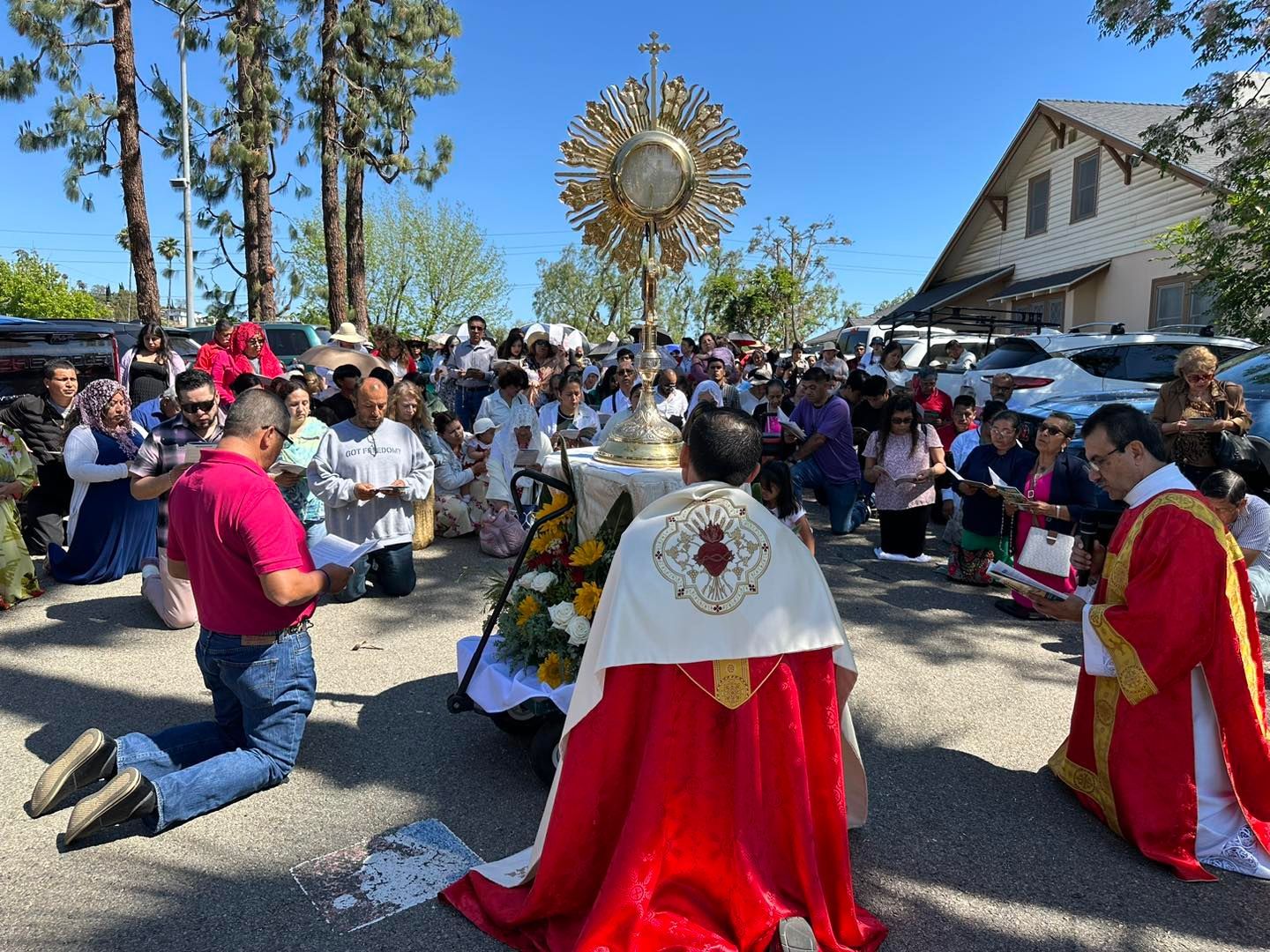 Outdoor religious ceremony with people kneeling before a decorated altar and a golden sunburst emblem