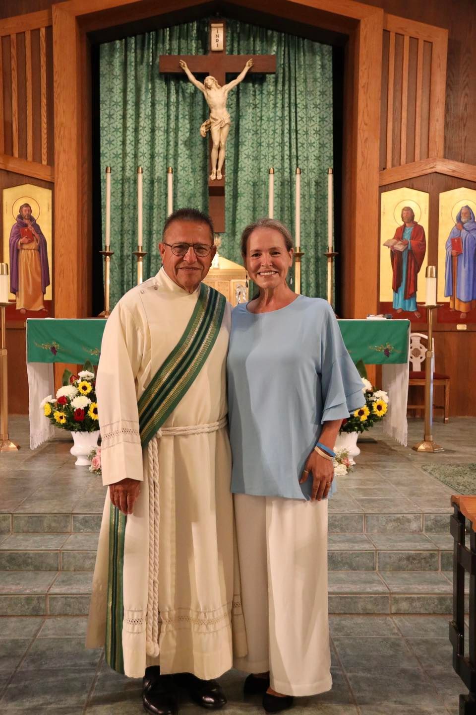 Two people standing before a church altar with a crucifix and green backdrop