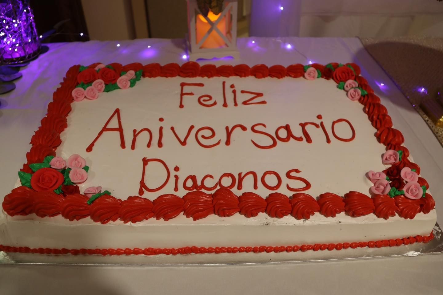 Celebration cake with red roses and the message “Feliz Aniversario Diaconos” on a table