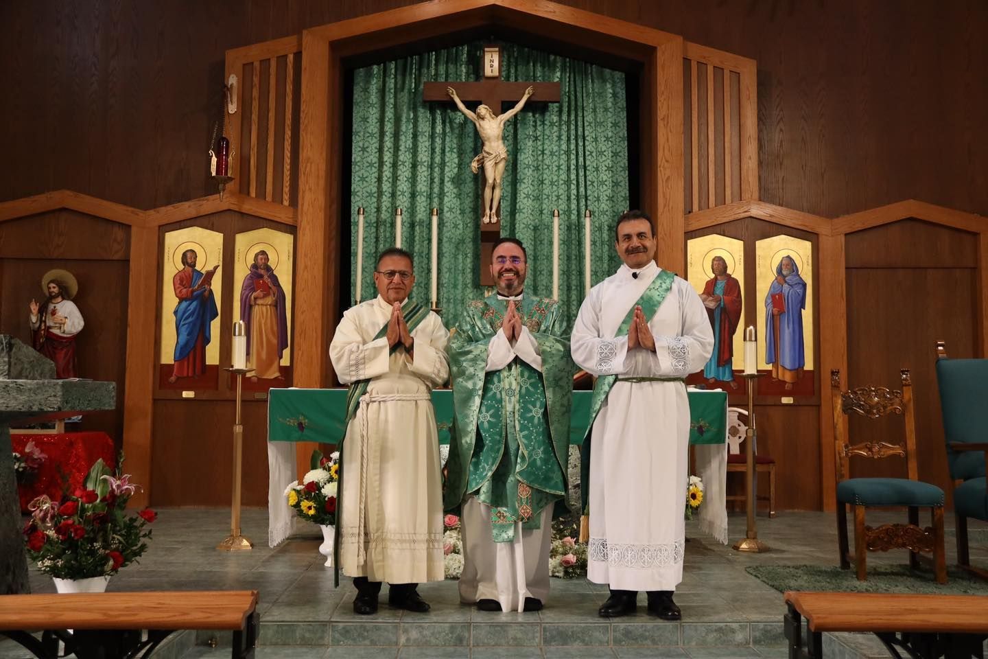 Three priests standing at a church altar, praying before a crucifix and green sanctuary backdrop.