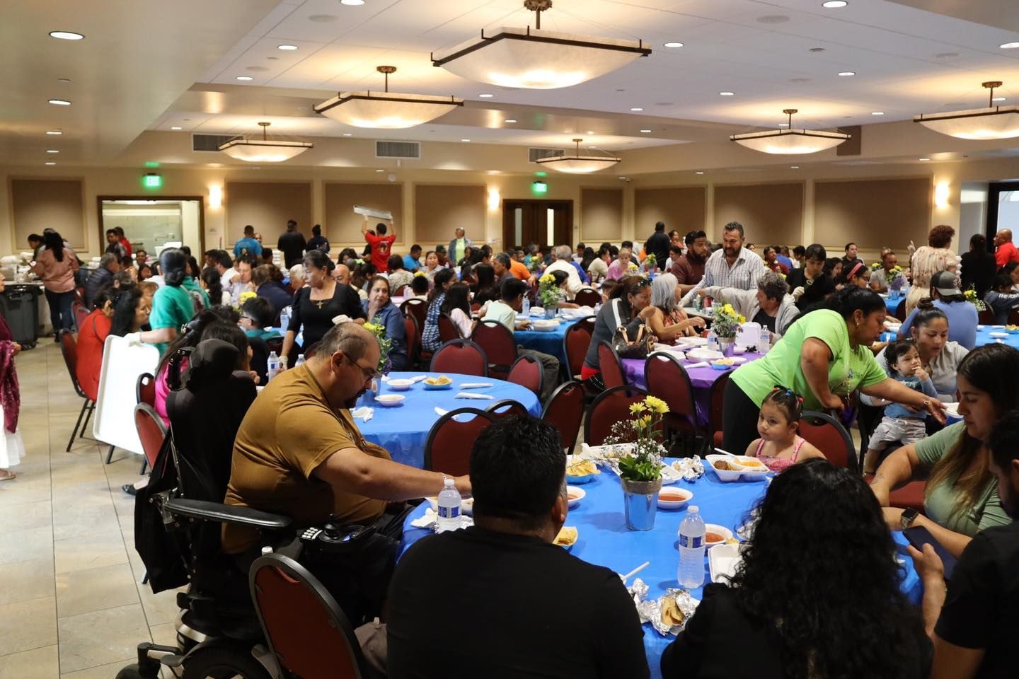 Banquet hall with many people seated at round tables during a large community meal
