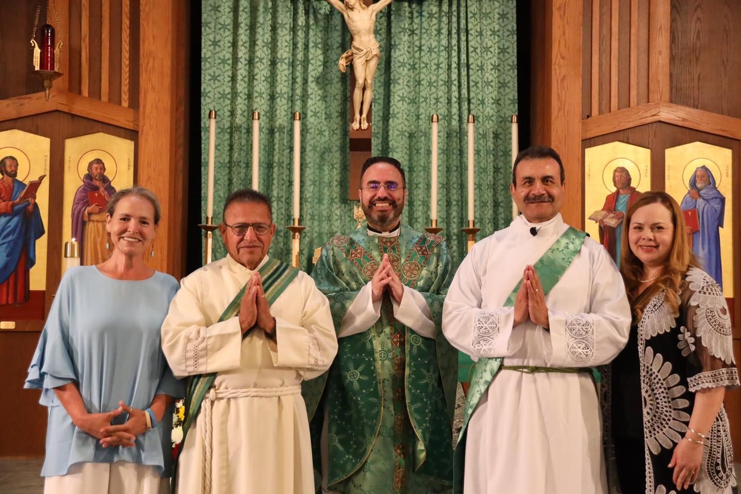 Five people pose in front of a church altar, with two priests in white robes centered between others.