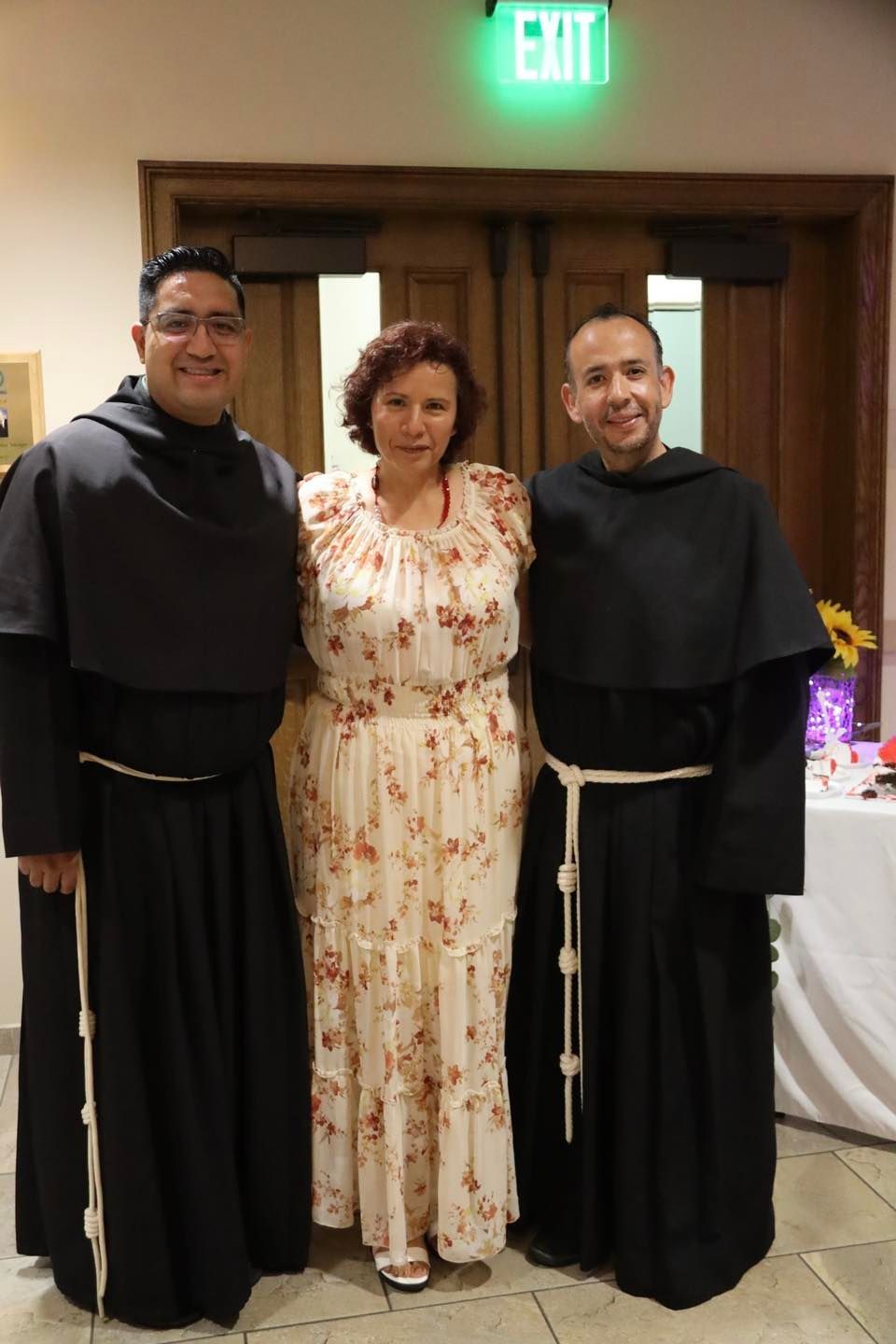 Three people posing indoors, with two in black robes and one in a floral dress.