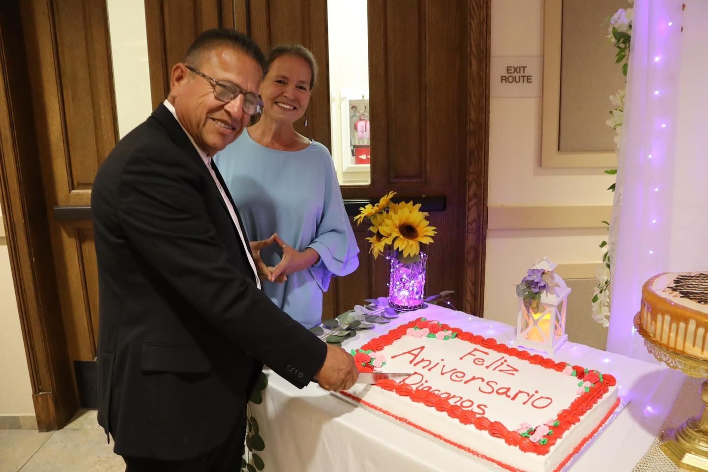 Two people cutting a white and red decorated cake at a party table.
