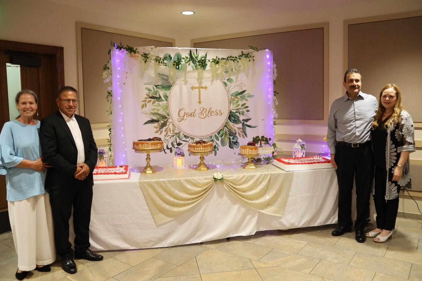 Guests posing beside decorated dessert table at a celebration with purple lights and gold drapery